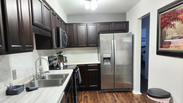 A modern kitchen with dark wood cabinets, stainless steel appliances, a marble countertop, and a wooden floor. - Awesome Condo in Central Raleigh (Raleigh)