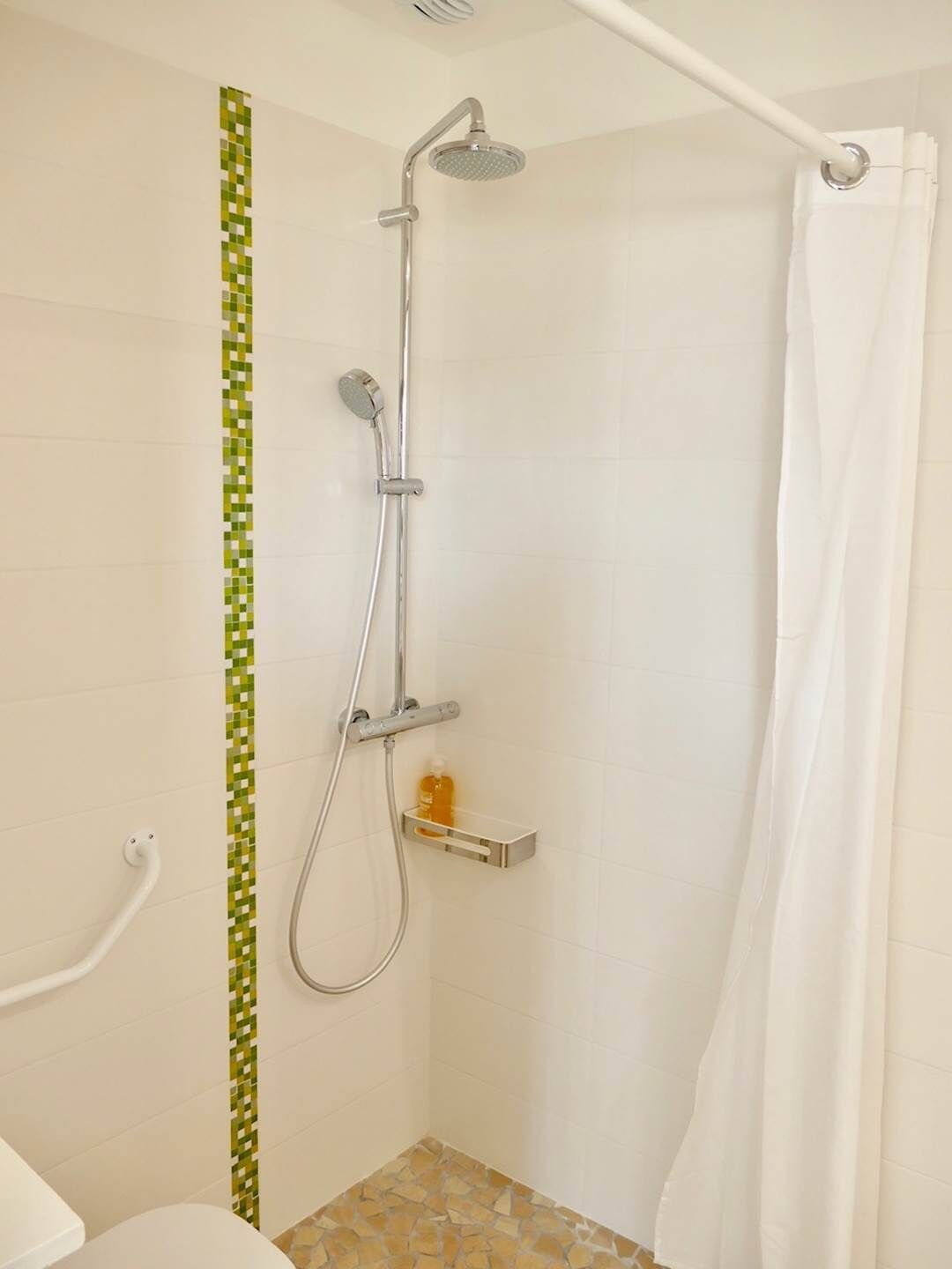 A shower with a handheld showerhead, a wall-mounted control, and a soap dish.