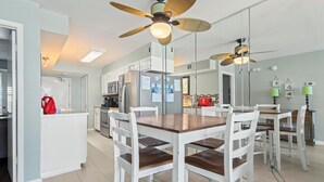 Uma cozinha moderna com armários brancos, uma ilha central e um espaço de refeições com mesa de madeira e cadeiras brancas.