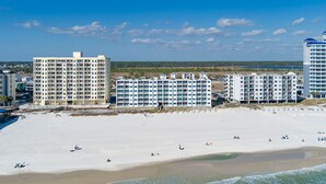 Um hotel à beira-mar com vários edifícios, uma praia de areia e um céu azul límpido.