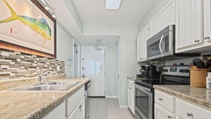 Cozinha moderna com armários brancos, bancadas de granito, uma grande pintura de peixe e vista para a sala de jantar.