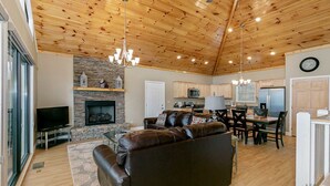 A spacious living area with a fireplace, leather sofa, dining table, and kitchen area.