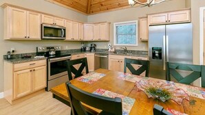 A kitchen with wooden cabinets, a stainless steel refrigerator, a microwave, an oven, and a dining table with chairs.