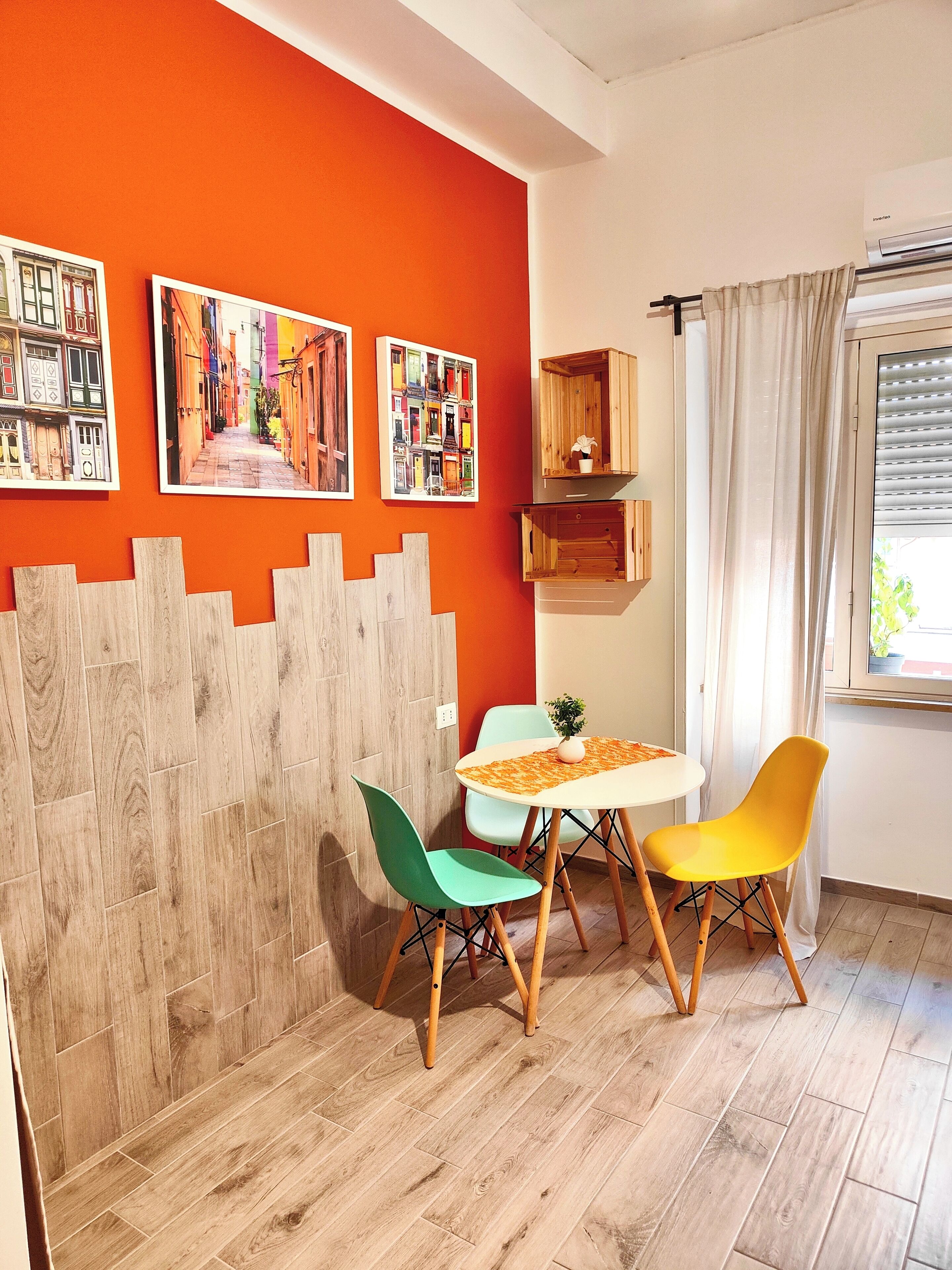 Een kamer met een houten vloer, een witte tafel, twee stoelen en een raam met gordijnen.