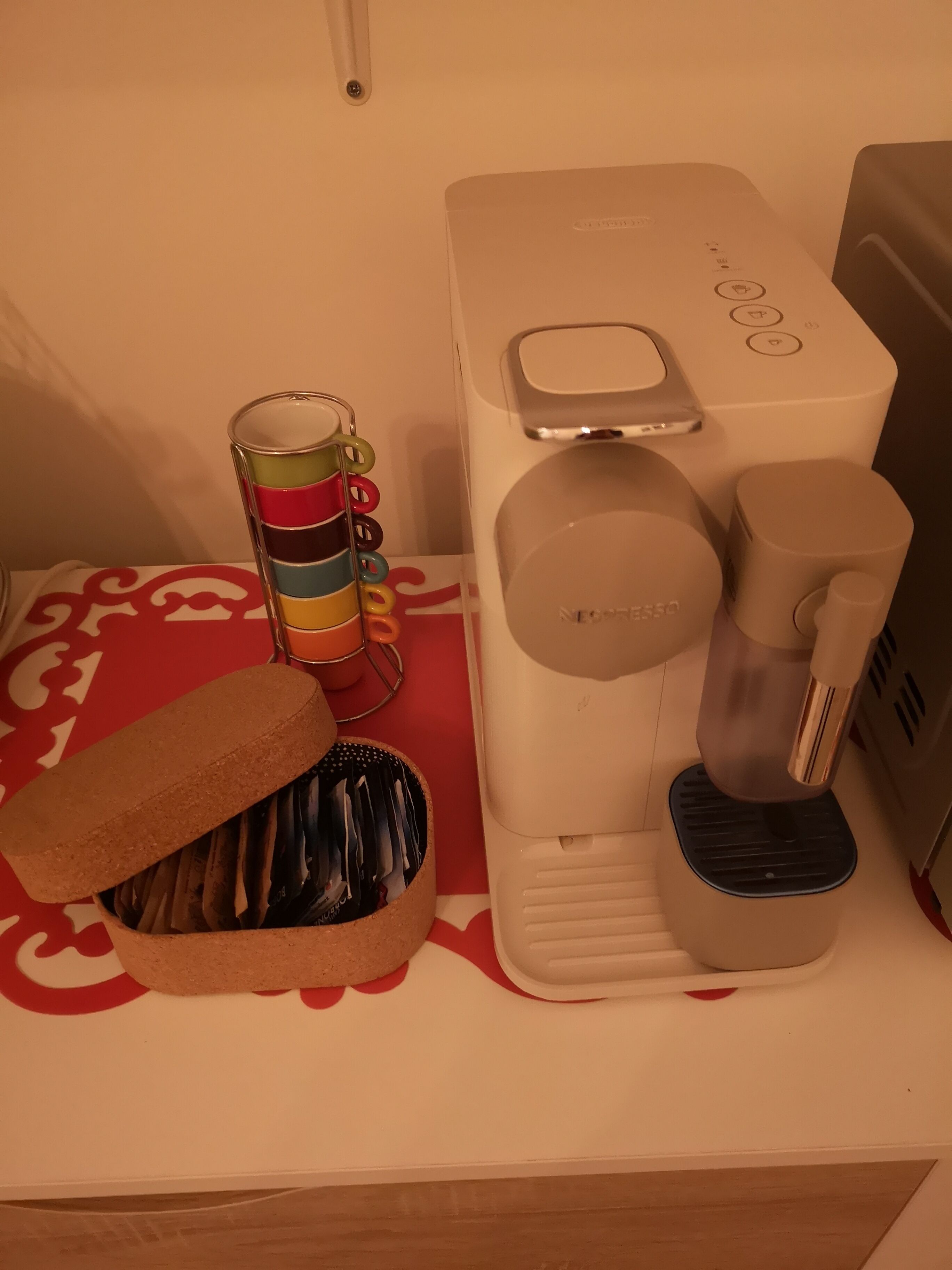 Una cafetera sobre una encimera con un portavasos y una cesta de revistas.