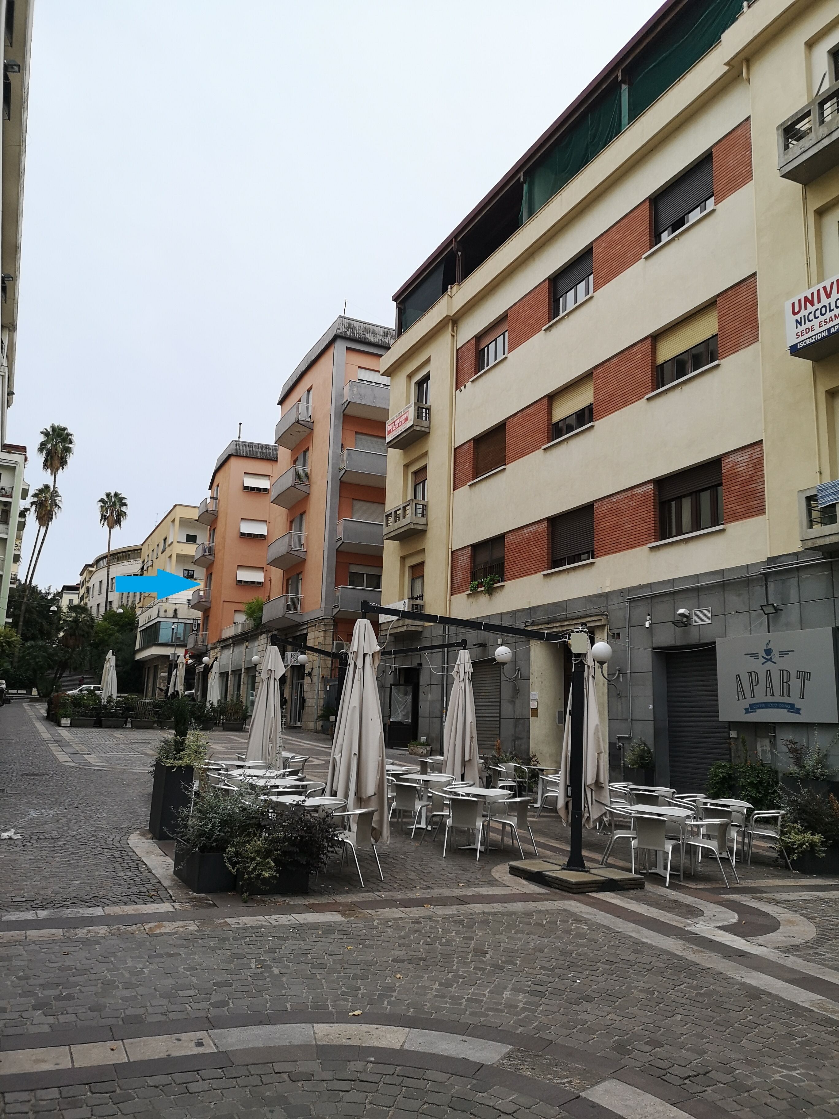 A street with outdoor seating, a building with a sign reading "UNIVERSITY," and another sign for "APART."