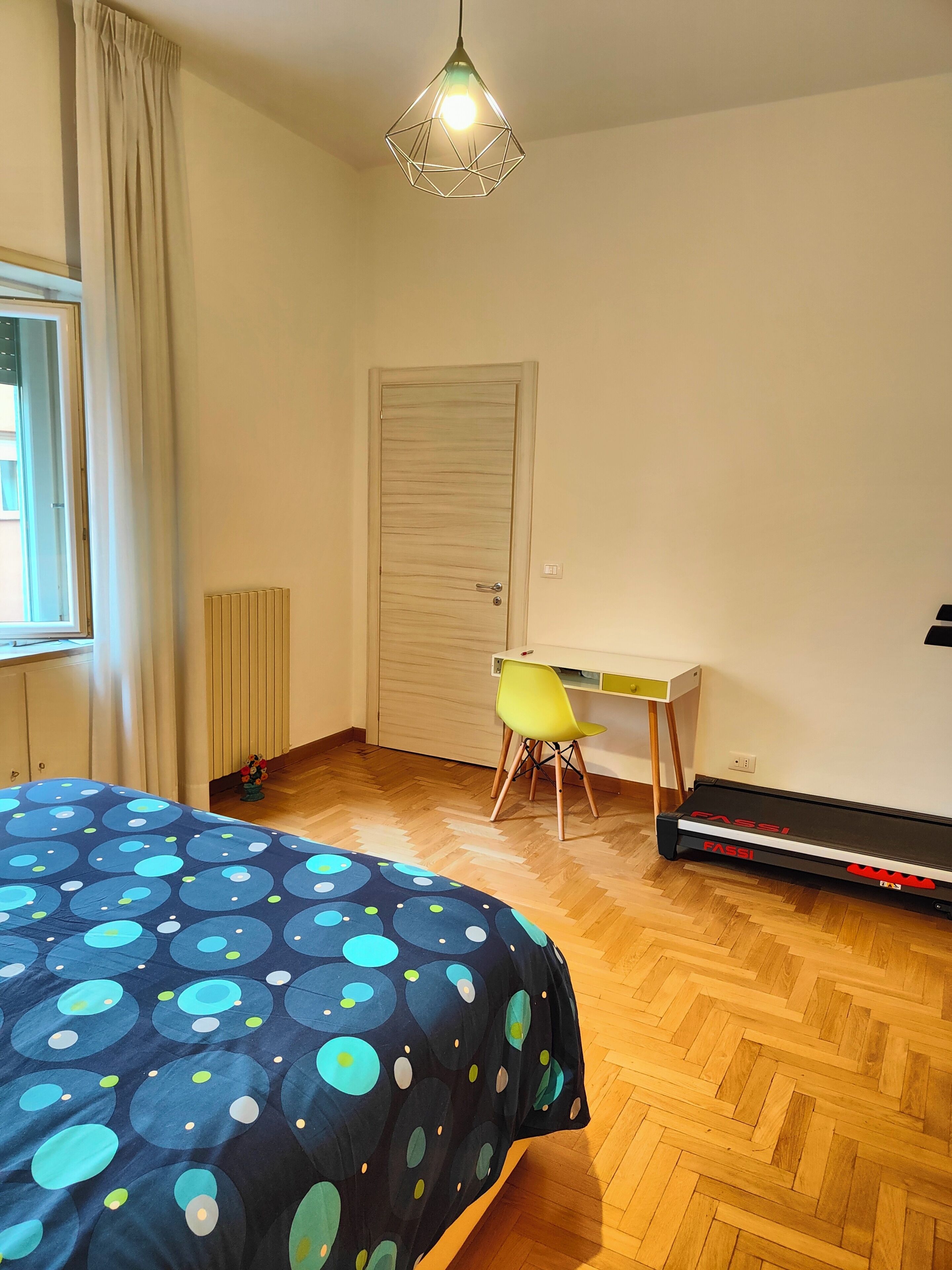 Ein Schlafzimmer mit Bett, Schreibtisch, Stuhl, Heizkörper und Laufband.