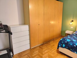 Un dormitorio con un armario de madera, una cinta de correr, una cama con edredón estampado y una mesita de noche con lámpara.