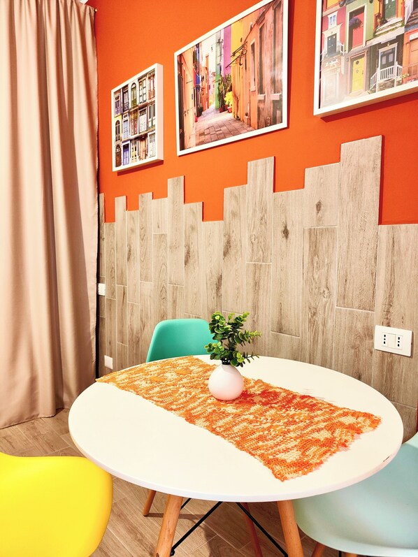 Una habitación con una mesa redonda, una planta en maceta y un tapete colorido.