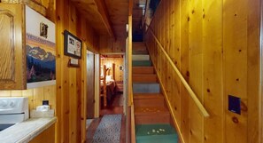 Un interior de madera con una zona de cocina, una escalera y un dormitorio visible al fondo.