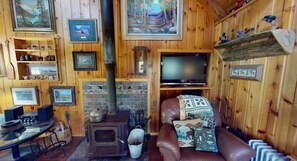 A cozy room with a fireplace, wooden walls, a television, and a leather couch.