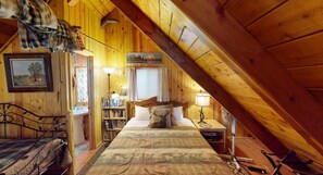 A cozy attic bedroom with a bed, bedside table, lamp, and a bookshelf.