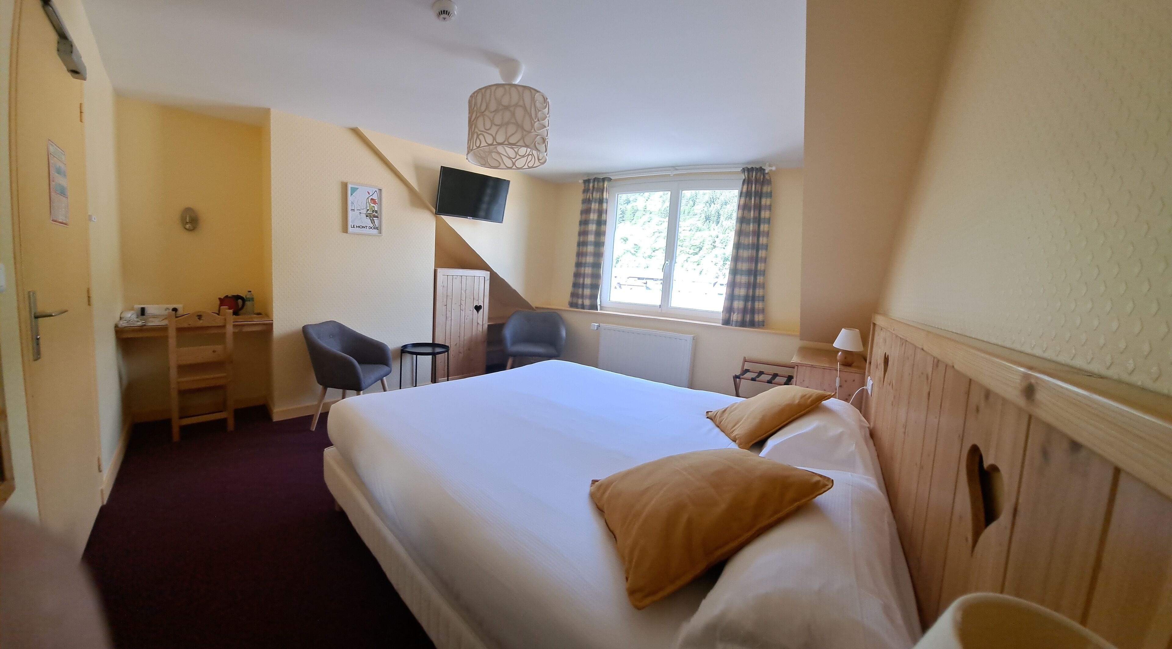 Habitación de hotel con cama, escritorio, silla y ventana con cortinas.