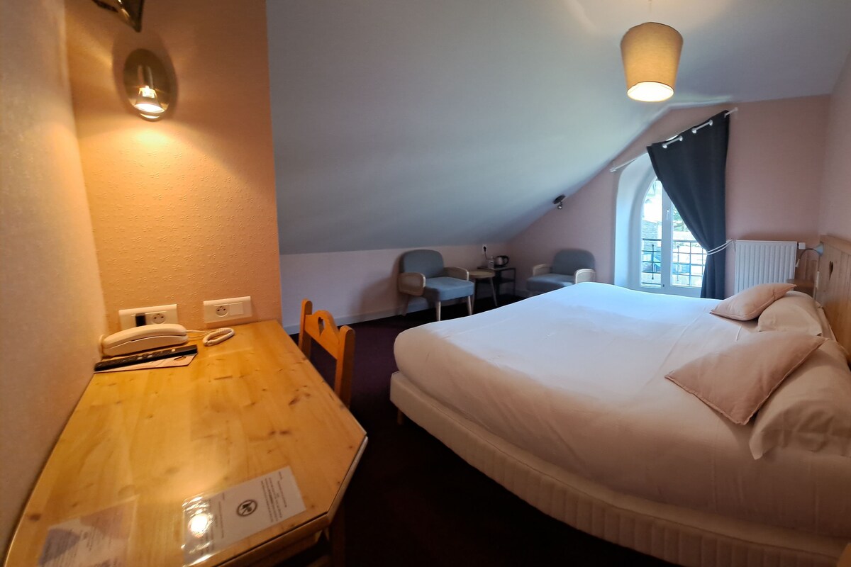 A bedroom with a bed, a desk, a chair, a small table, and a window with curtains.