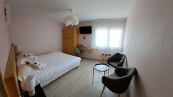 Un dormitorio con cama, escritorio, dos sillas, televisor y ventana con cortinas.