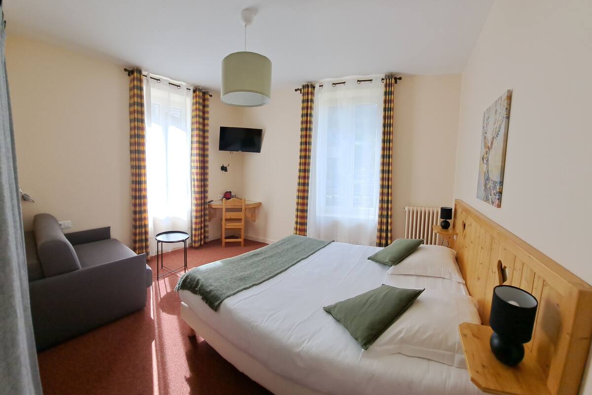 A hotel room with a bed, a desk, a chair, a TV, and a painting on the wall.