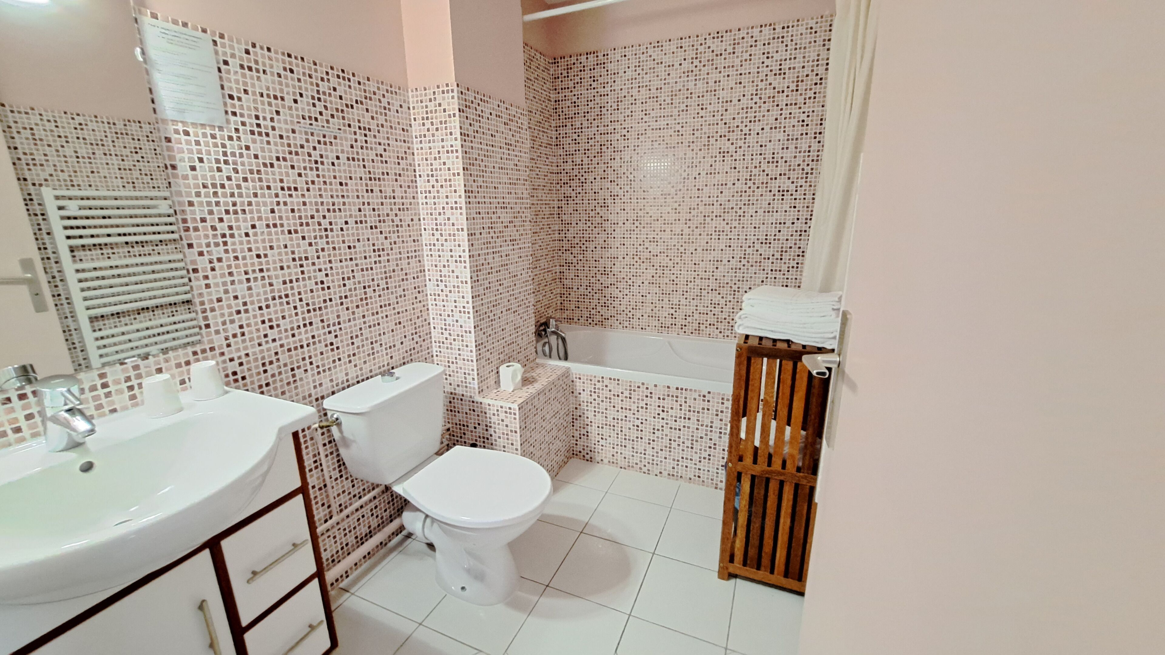 Une salle de bain comprenant des toilettes, un lavabo et une baignoire, le tout recouvert de carreaux formant un motif en mosaïque.