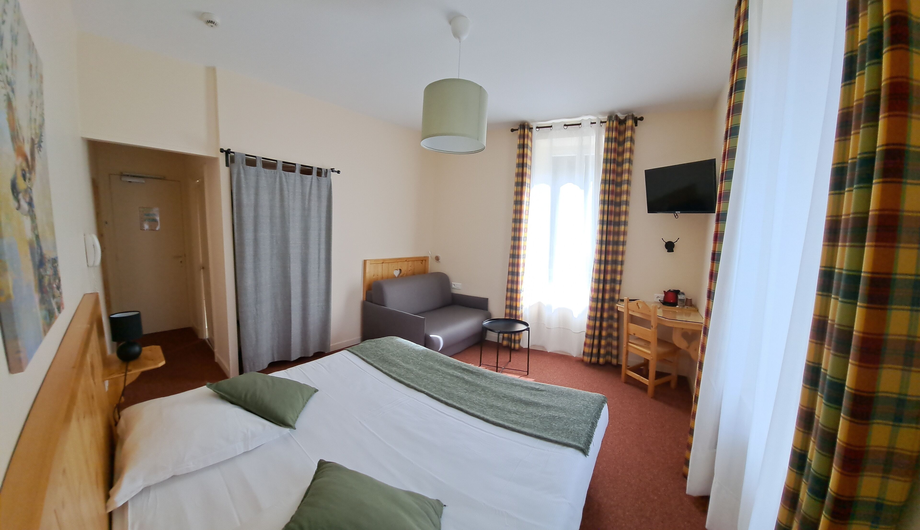 Hotelkamer met een bed, een slaapbank, een bureau, een stoel, een televisie en een raam met gordijnen.