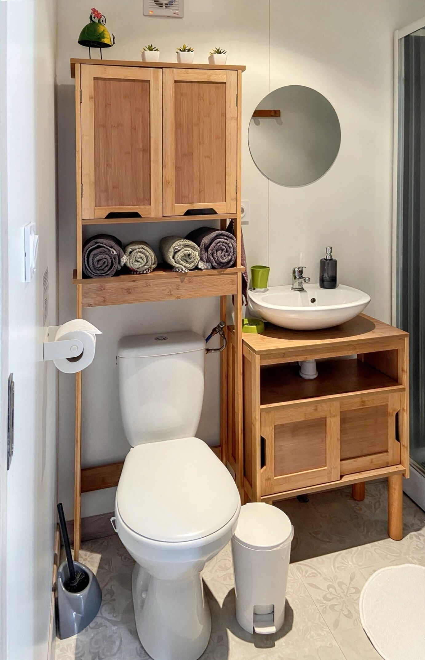 Un baño con inodoro, lavamanos, espejo y un armario de madera con toallas.