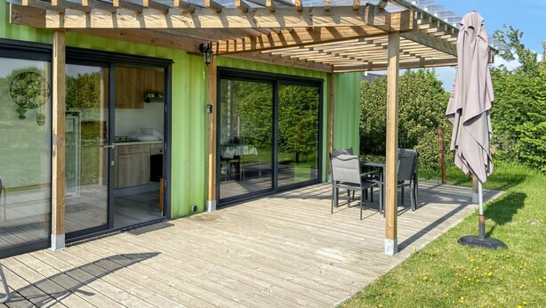 Een modern huis met een overdekt terras, grote schuifpuien en een houten terras.