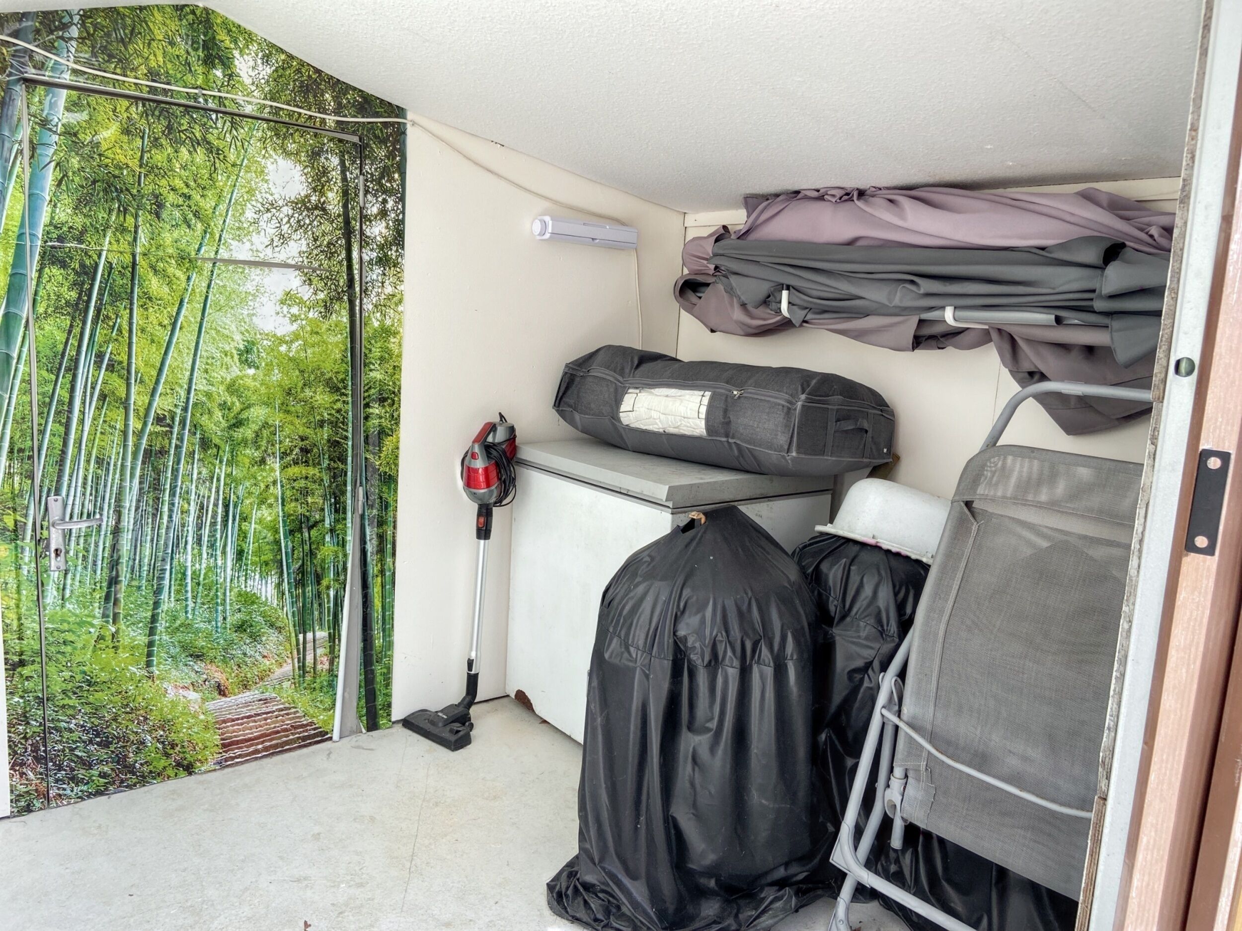 Ein Zimmer mit Blick auf einen Bambuswald, ein Staubsauger, ein Klappsessel und eine Ablagebank.