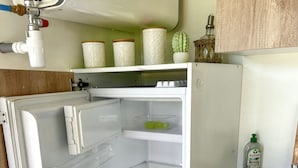 Een open koelkast met heldere planken, een waterdispenser en een spoelbak met afwasmiddel.