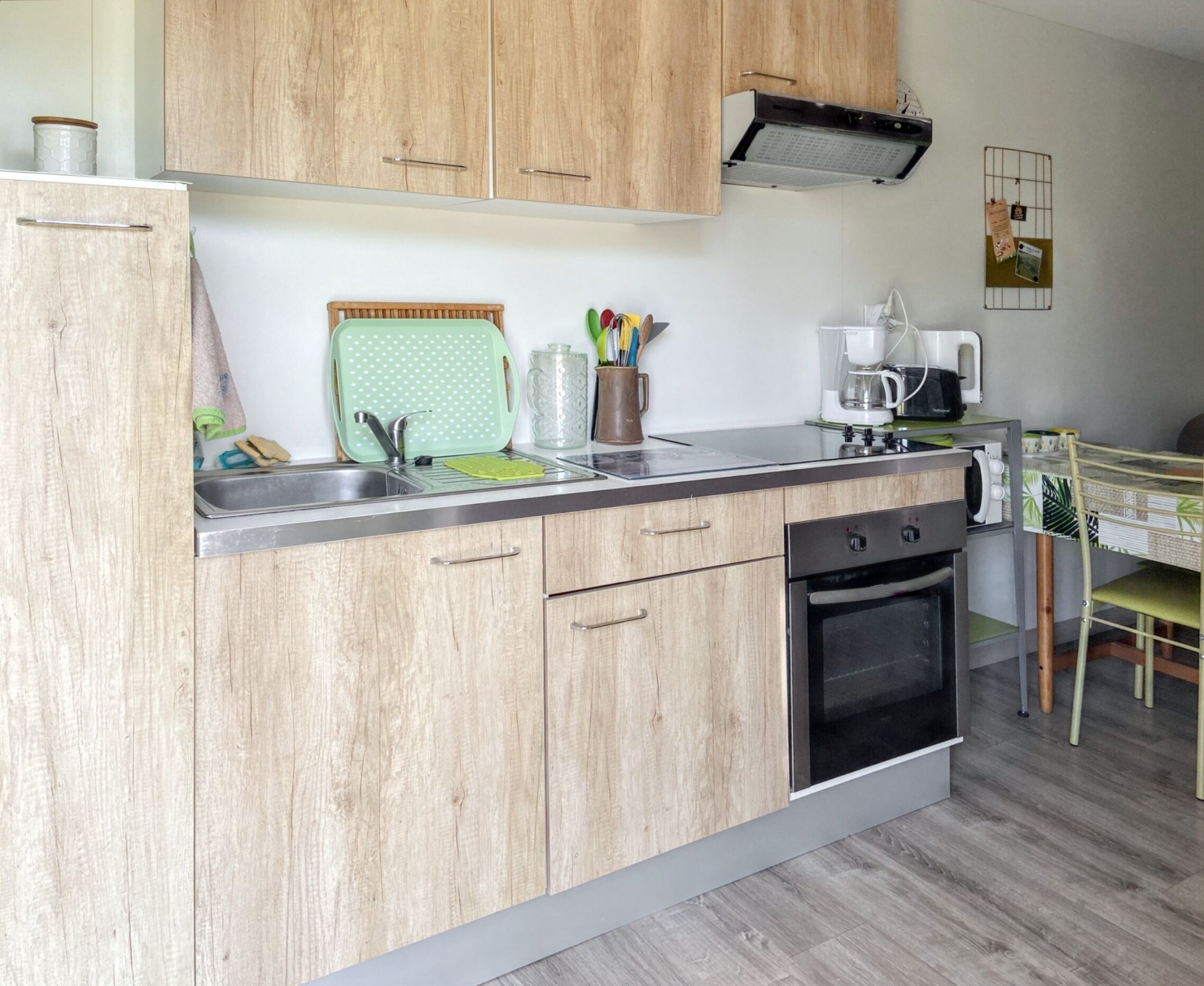 A compact kitchen with wooden cabinets, a built-in oven, a coffee maker, and a drying rack.