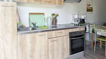 A compact kitchen with wooden cabinets, a built-in oven, a coffee maker, and a drying rack.
