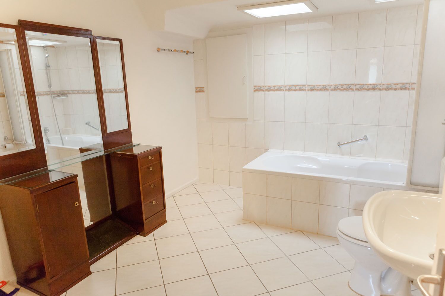 A bathroom with a glass-enclosed vanity, a freestanding bathtub, a toilet, and a sink.
