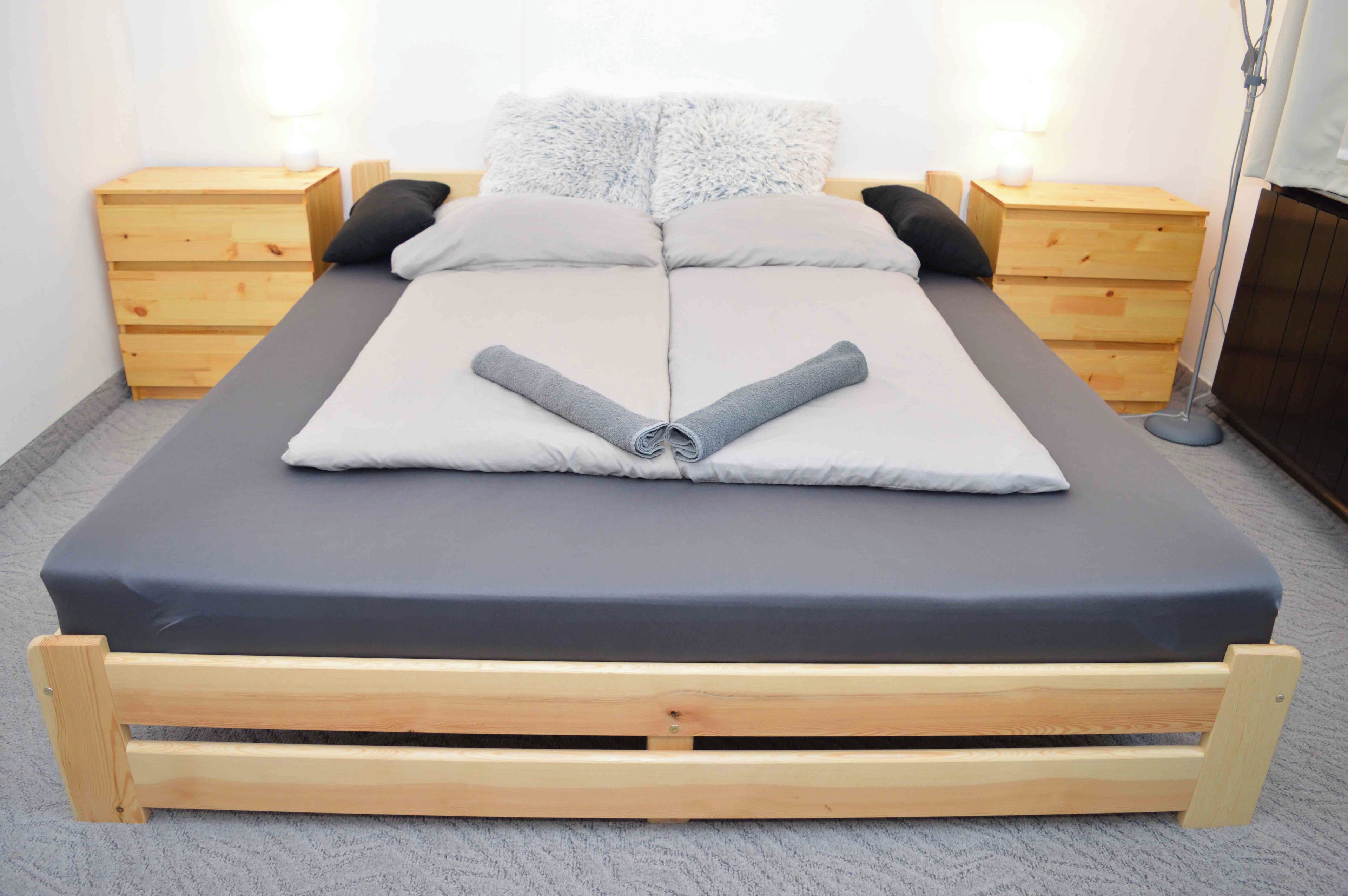 Una cama con colchón gris, cabecera de madera y dos mesitas de noche con lámparas.