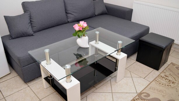 A modern living room with a grey sofa, a glass coffee table, and a white vase with pink flowers. - Lorabel Apartmanház Hévíz (Hévíz)