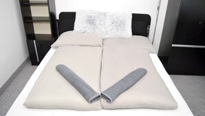 A neatly made bed with a white mattress, two beige pillows, and two rolled gray towels. - Lorabel Apartmanház Hévíz (Hévíz)