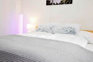 A neatly made bed with white linens and fluffy pillows, a bedside lamp, and a wall with three framed pictures.