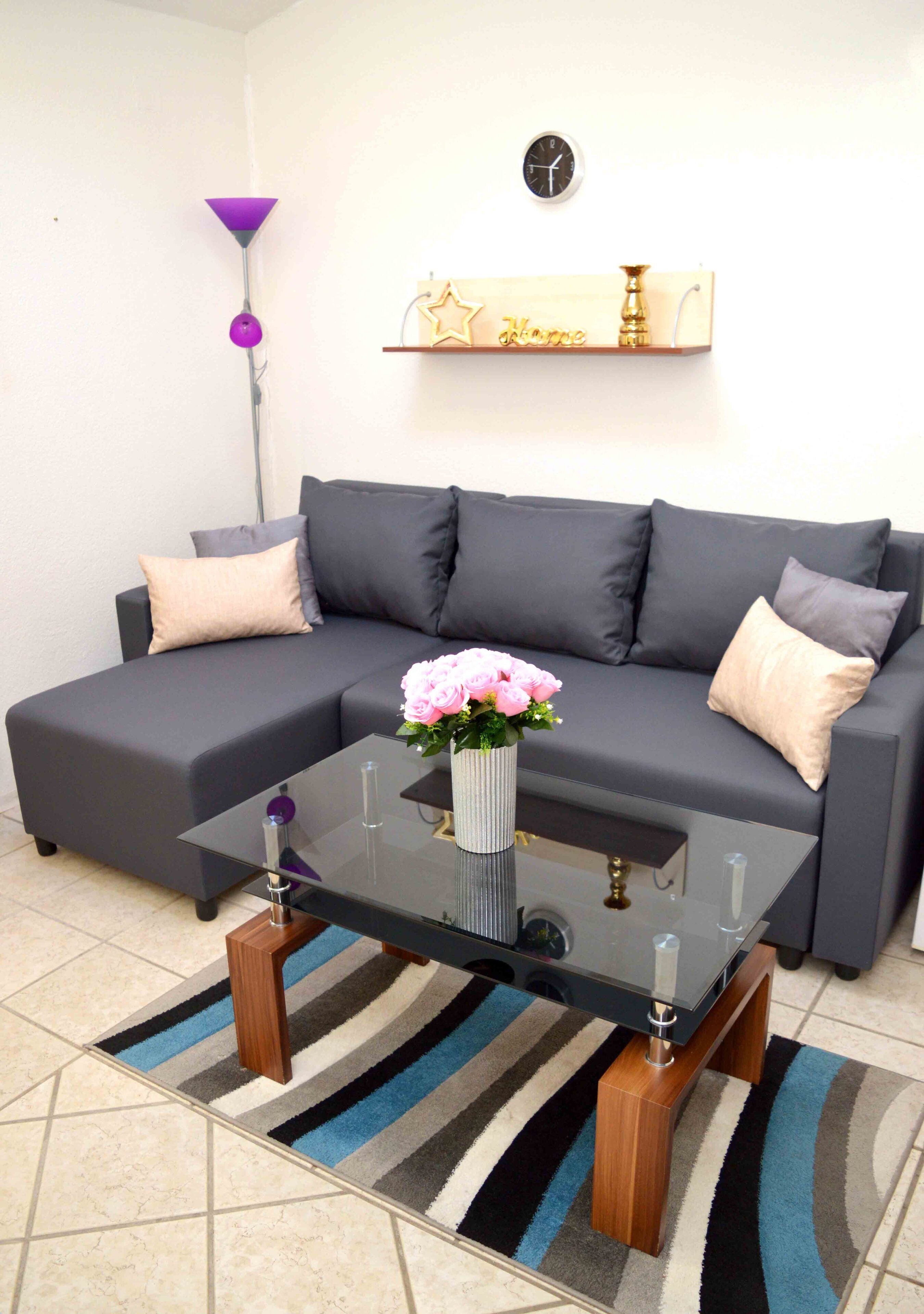 A modern living room with a grey sectional sofa, a glass coffee table, and a striped rug.