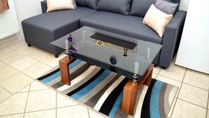 A modern living room with a dark grey sectional sofa, a glass coffee table with wooden legs, and a striped area rug. - Lorabel Apartmanház Hévíz (Hévíz)