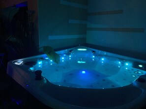 A hot tub with multiple jets and a control panel, surrounded by a dark room with minimal lighting.