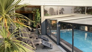 A modern outdoor pool area with a glass enclosure, lounge chairs, and potted plants. - Desir'Add (La Clisse)