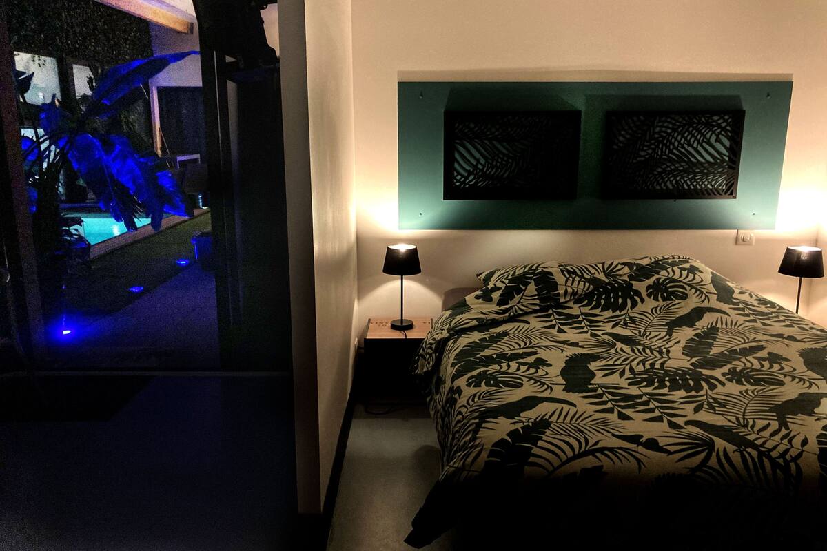 Une chambre à coucher avec un lit, deux lampes fixées au mur et une fenêtre donnant sur une piscine.