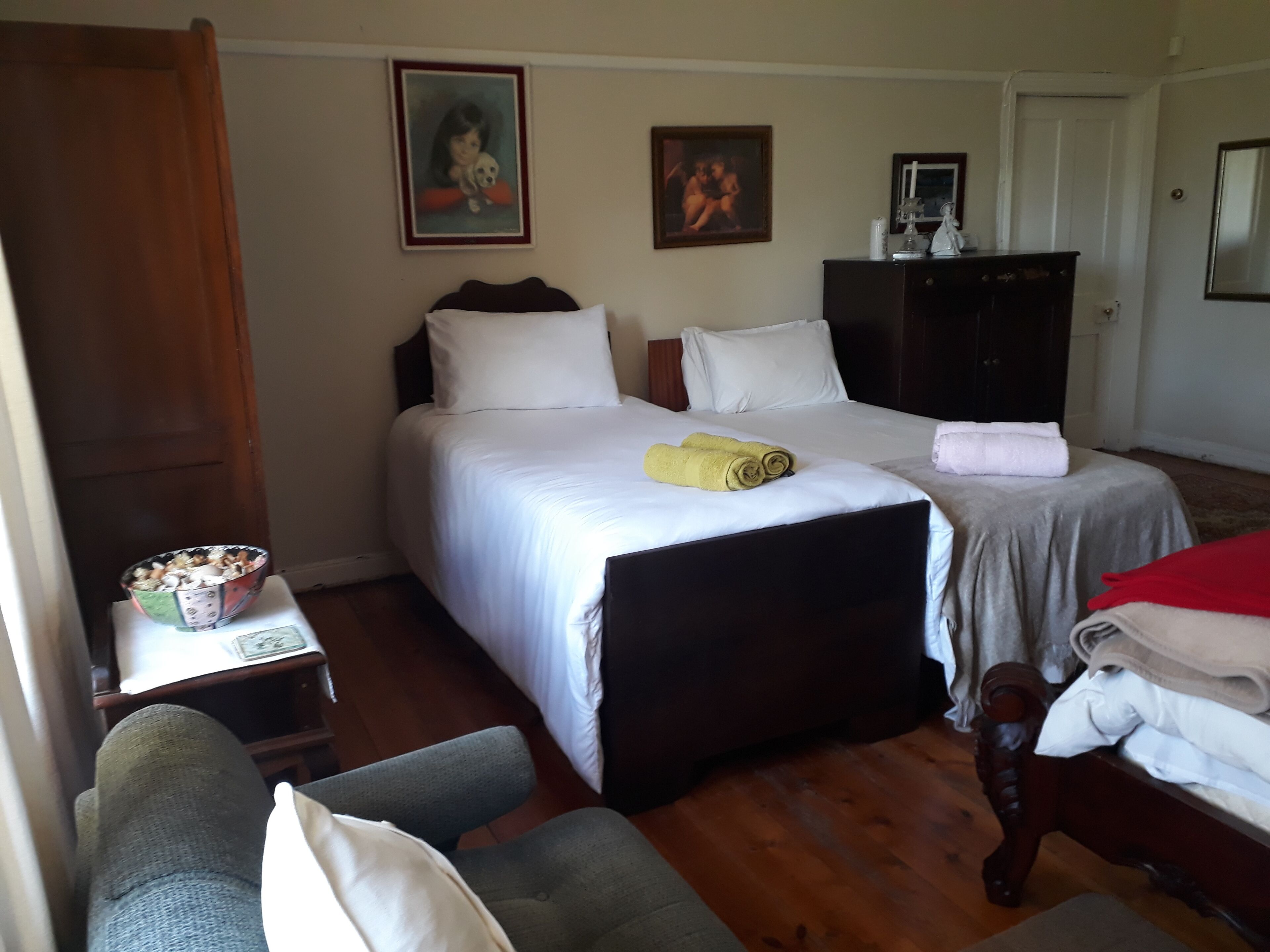 A hotel room with a bed, a desk, a chair, a dresser, and two paintings on the wall.