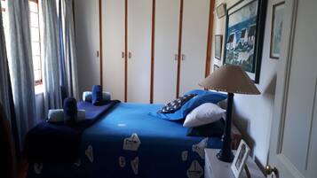 A bedroom with a bed, a nightstand, a lamp, a wardrobe, and a window with curtains.