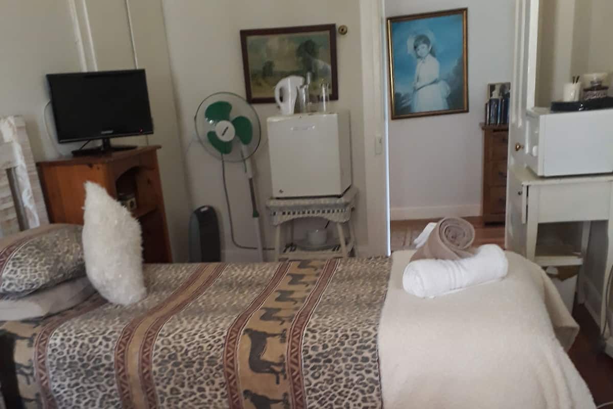 A hotel room with two beds, a television, a small table, a fan, and a painting on the wall.
