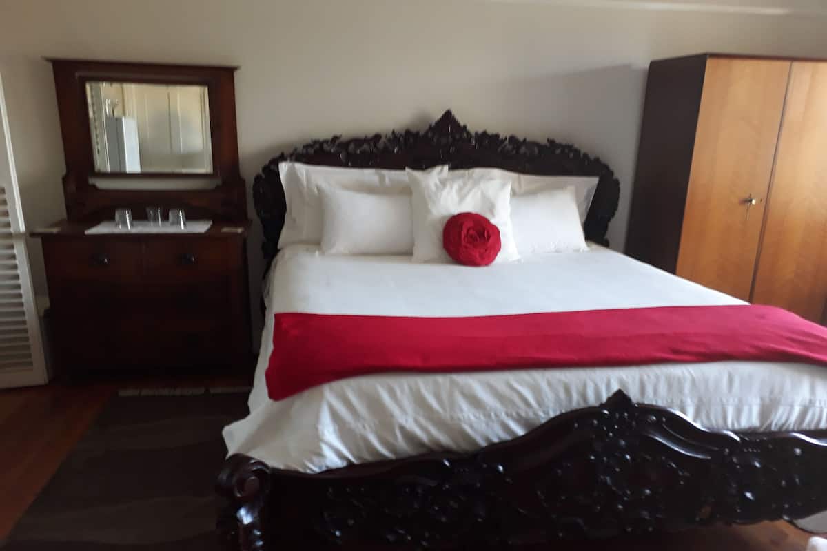 A bedroom with a bed, a wooden dresser, a wardrobe, and a mirror.