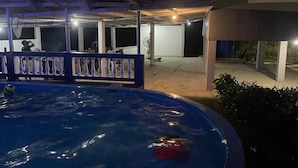A swimming pool with a covered area and a building in the background.