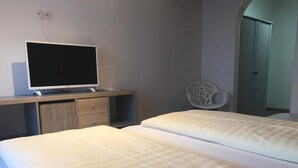 Una habitación de hotel con una cama, un televisor sobre un mueble, un armario y una silla.