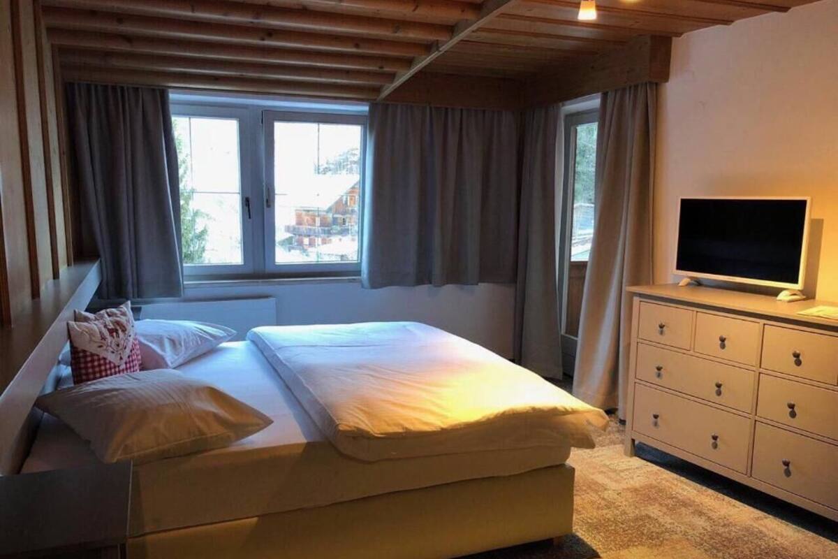 A bedroom with a bed, a dresser, a television, and a window with curtains.