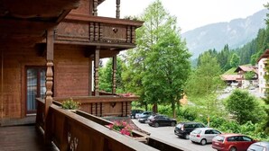 Un balcón de madera con vista a coches estacionados y vegetación al fondo.