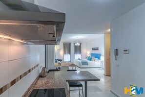 Ett modernt kök med en inbyggd spis, en matplats med bord och stolar samt ett vardagsrum med en soffa och en tv.
