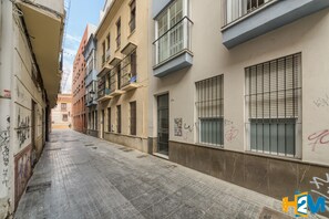 A narrow urban street with buildings on both sides, featuring balconies, windows, and some graffiti.