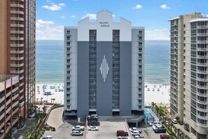 A hotel with a prominent logo, a parking lot, and a beach view.