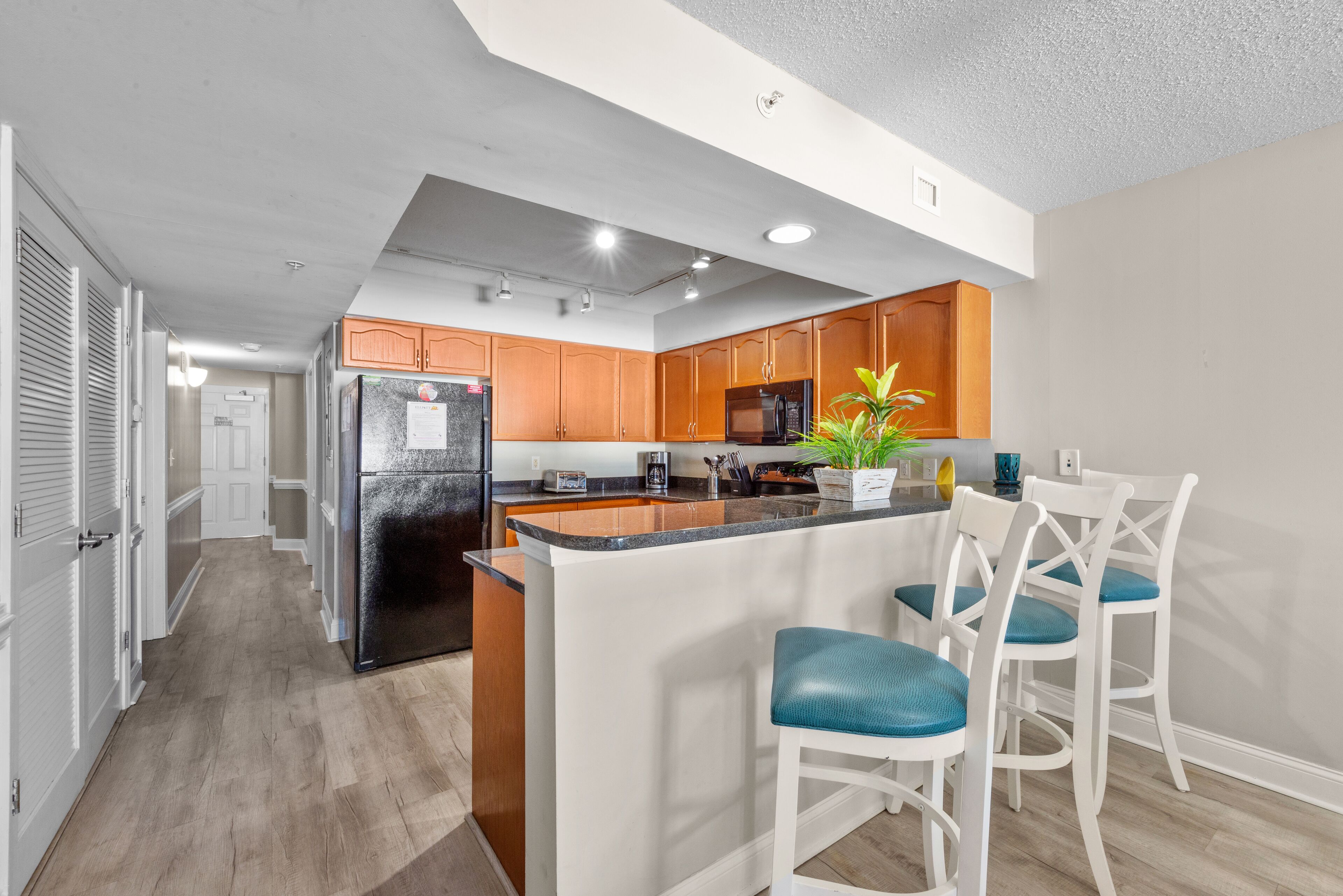 A modern kitchen with wooden cabinets, a black refrigerator, and a central island with bar stools.